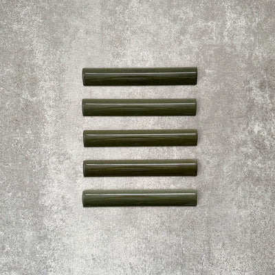 Flat lay of Zellige Botanical Green Bullnose 3 × 20cm Moroccan-style ceramic trim tiles in deep botanical green tones, displayed with a smooth rounded edge and glossy glaze, arranged on a textured grey background to highlight the handcrafted zellige-effect finish and decorative edging profile.
