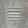 Flat lay of Zellige Aqua 3×20cm Moroccan-style ceramic bullnose tiles, showcasing the rounded edge profile, glossy blue-green glaze and subtle tonal variation on a neutral background.