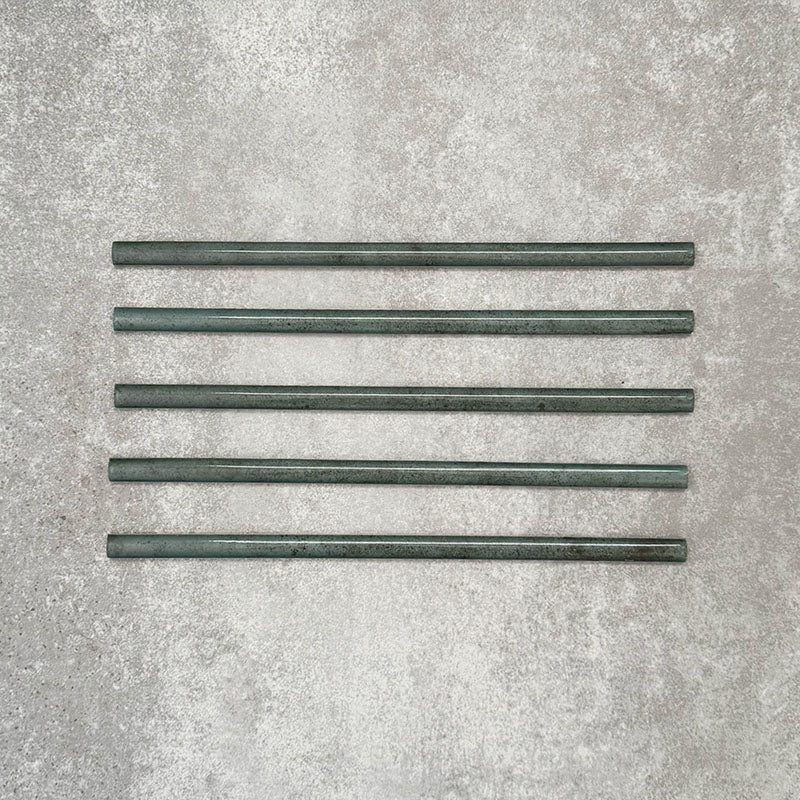 Allegra Green Gloss pencil bullnose border tiles in a 1.2 × 30cm ceramic format, shown as five pieces laid horizontally to display the slim profile, rounded edges, tonal green variation and glossy glazed finish on a neutral textured background.