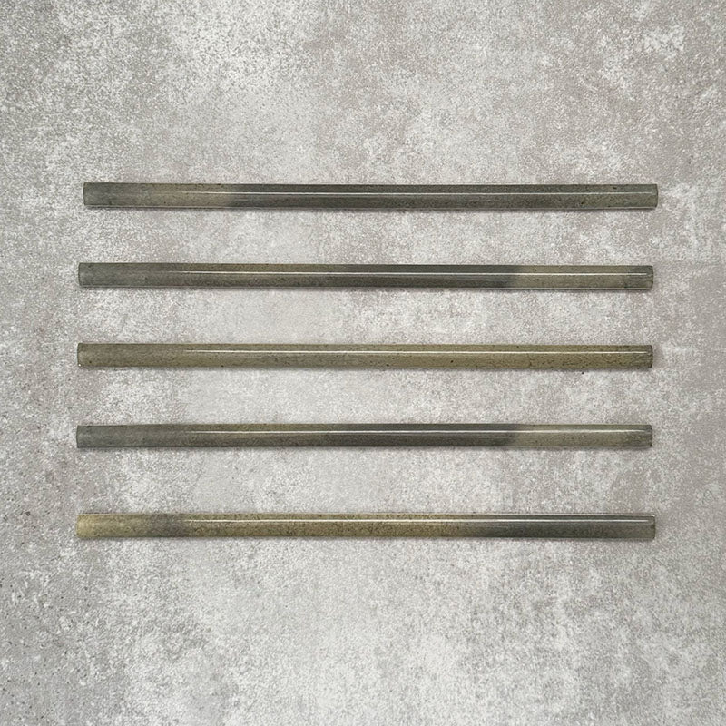 Five Allegra Daisy Green Gloss pencil bullnose border ceramic tiles in a 1.2 × 30cm format, laid horizontally to showcase the slim profile, glossy finish and subtle natural green tonal variations across the set.