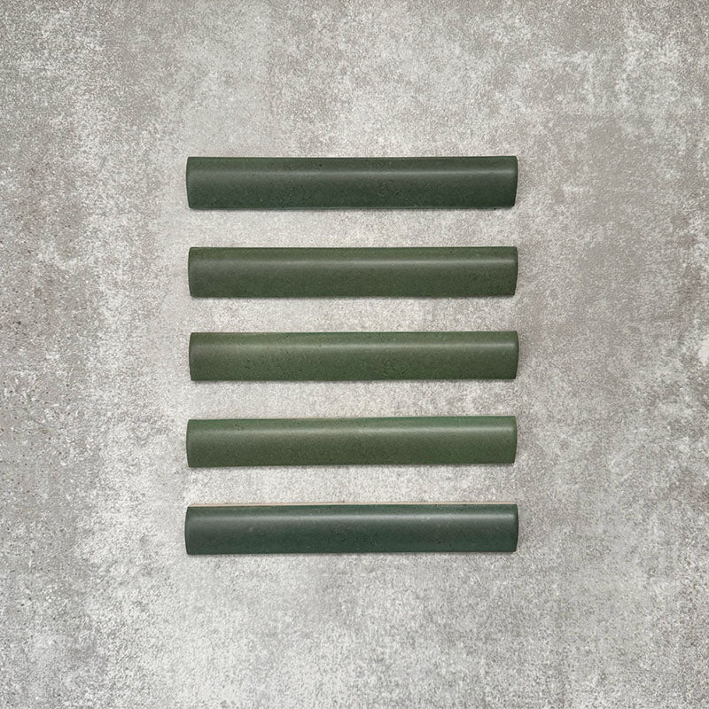 Flat lay of Zellige Malachite Green 3×20cm Moroccan-style ceramic bullnose tiles, showcasing the rounded edge profile, rich green glaze and subtle tonal variation on a neutral background.