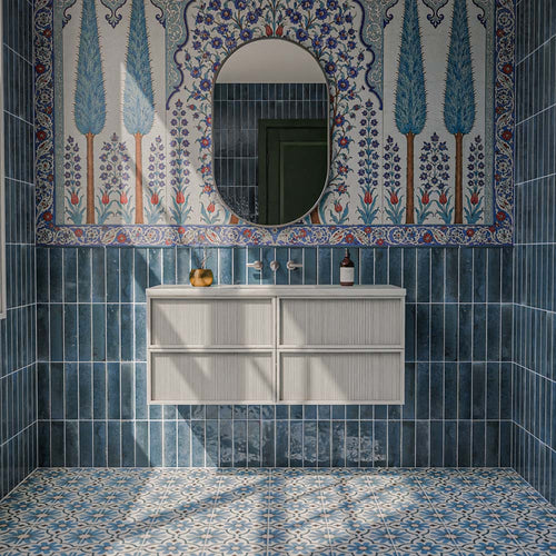 Allegra Blue 6cm x 25cm gloss brick wall tiles, featuring rich blue tonal variation throughout a statement bathroom, paired with intricate blue patterned floor tiles and a decorative floral mural.