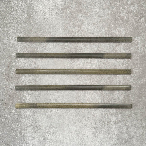 Five Allegra Daisy Green Gloss pencil bullnose border ceramic tiles in a 1.2 × 30cm format, laid horizontally to showcase the slim profile, glossy finish and subtle natural green tonal variations across the set.
