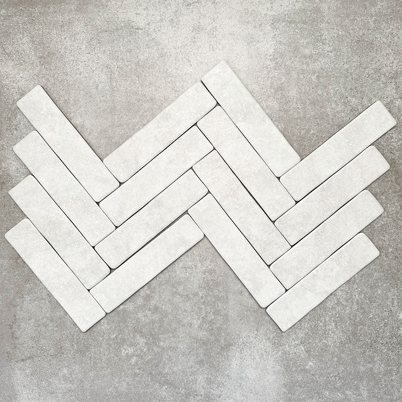 Product image of Amalfi Brick Carrara Vintage Marble wall and floor tiles in a 5.4cm x 22cm format, arranged in a herringbone pattern, showcasing a soft white marble effect surface with subtle tonal variation.