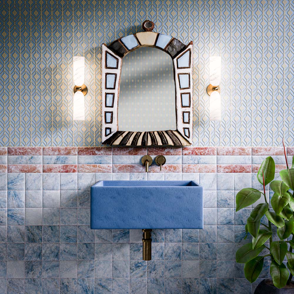 Bathroom featuring Amalfi Brick Rouge Vintage Marble 5.4x22cm wall tiles installed vertically, combining soft blue and blush-red marble-effect tones for a distinctive vintage look. The decorative border detail, statement blue basin, brass fixtures and patterned wallpaper create a colourful, Mediterranean-inspired space full of character, texture and timeless charm.