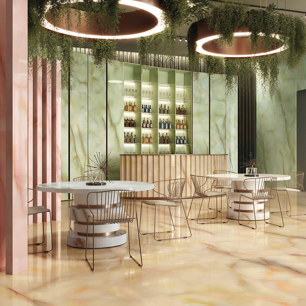 Restaurant interior featuring Anastasia Jade Green Onyx Matt 60 × 120cm stone effect floor and wall tiles, with soft green tones and flowing gold veining, paired with round tables, metallic chairs, and statement ceiling lighting.