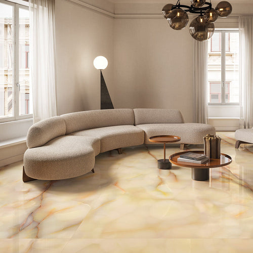 Living room featuring Anastasia Miele Onyx Matt 60 × 120cm stone effect floor tiles, with warm honey tones and soft veining, paired with a curved sofa, wooden tables, soft lighting, and large windows.