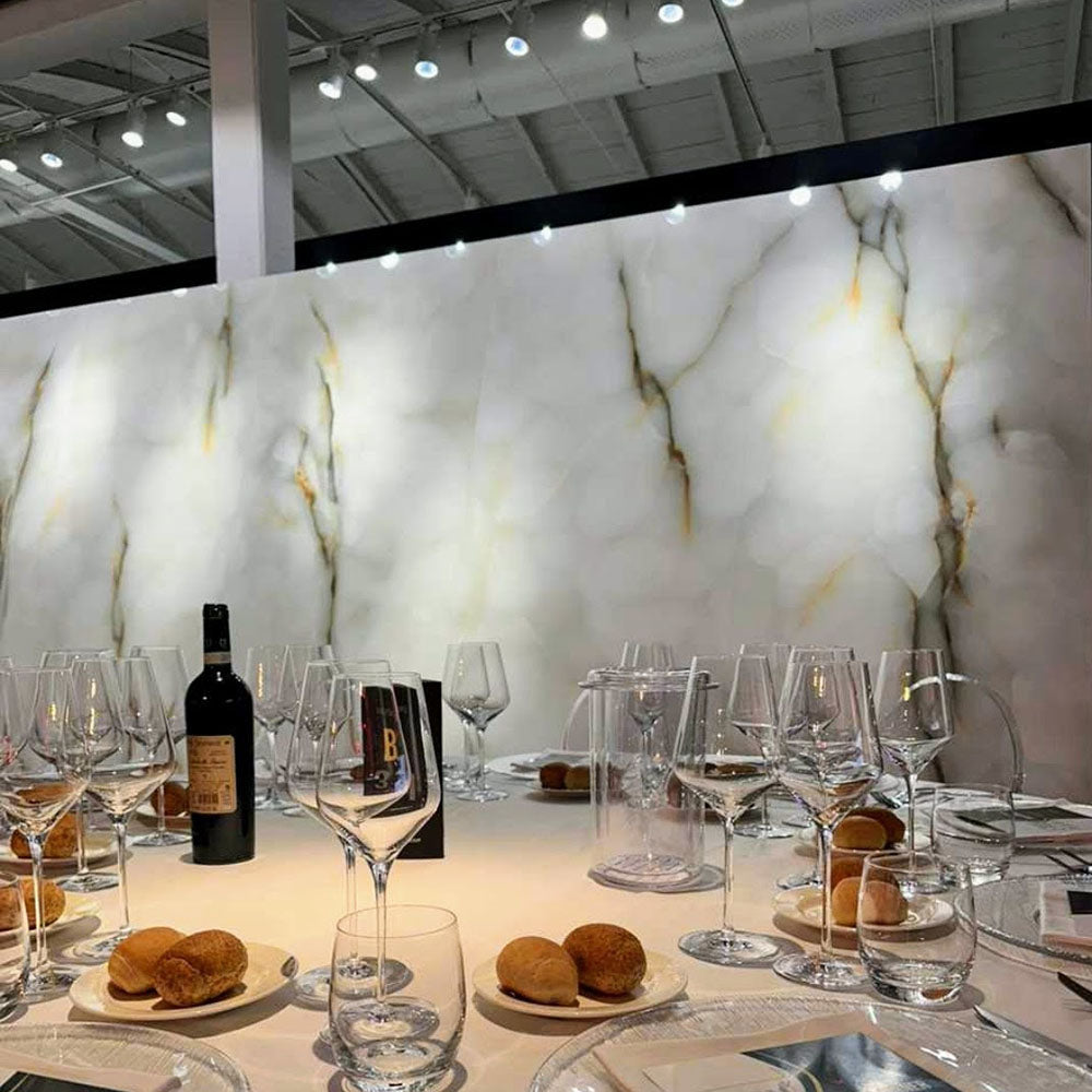 Dining setting featuring Anastasia Turchese Blue Onyx Matt 60 × 120cm stone effect wall tiles, with soft blue tones and flowing gold veining, paired with a dressed table, glassware, and warm overhead lighting.