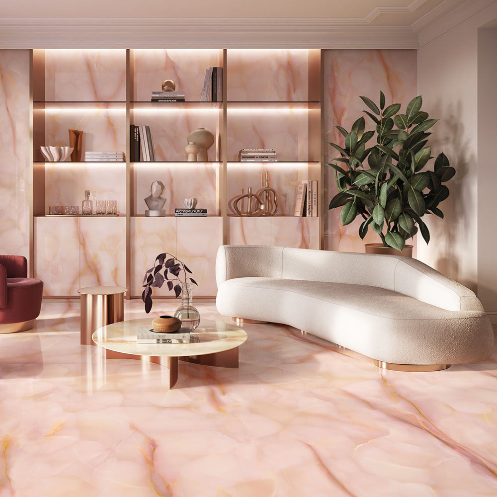 Living room featuring Anastasia Rose Onyx Polished 60 × 120cm stone effect floor and wall tiles, with soft pink tones and delicate gold veining, paired with curved seating, warm lighting, and built-in shelving.