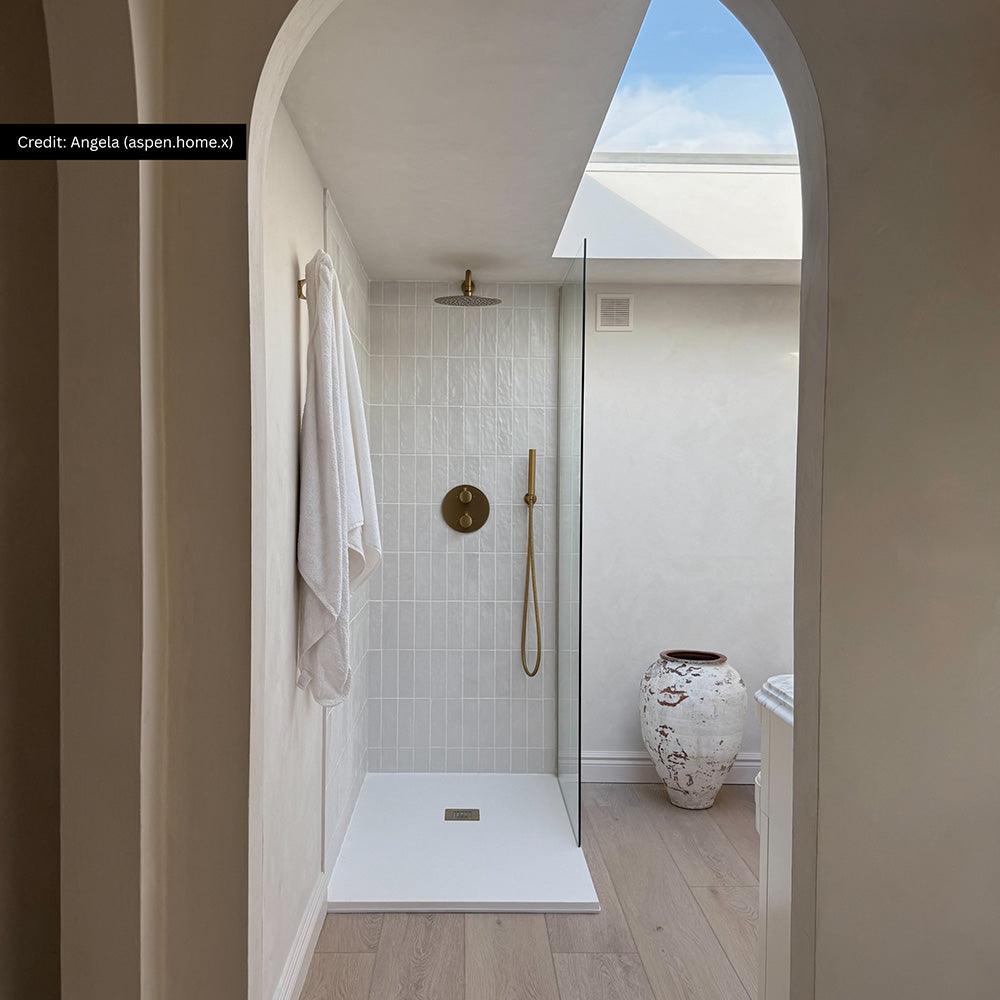 Bathroom interior featuring Zellige Oyster Brick 6.5x20cm Moroccan style tiles in soft neutral tones, installed vertically in a walk-in shower, styled with brass shower fittings, glass screen and natural textures in a calm contemporary space.