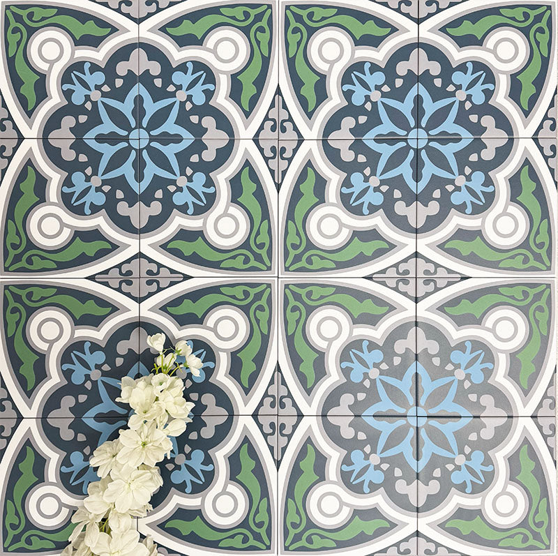 Group of London Streets Baker Street 20x20cm Victorian Moroccan style porcelain tiles arranged to showcase the repeating blue, green, grey and white geometric pattern, styled with white flowers in a decorative flat-lay setting.