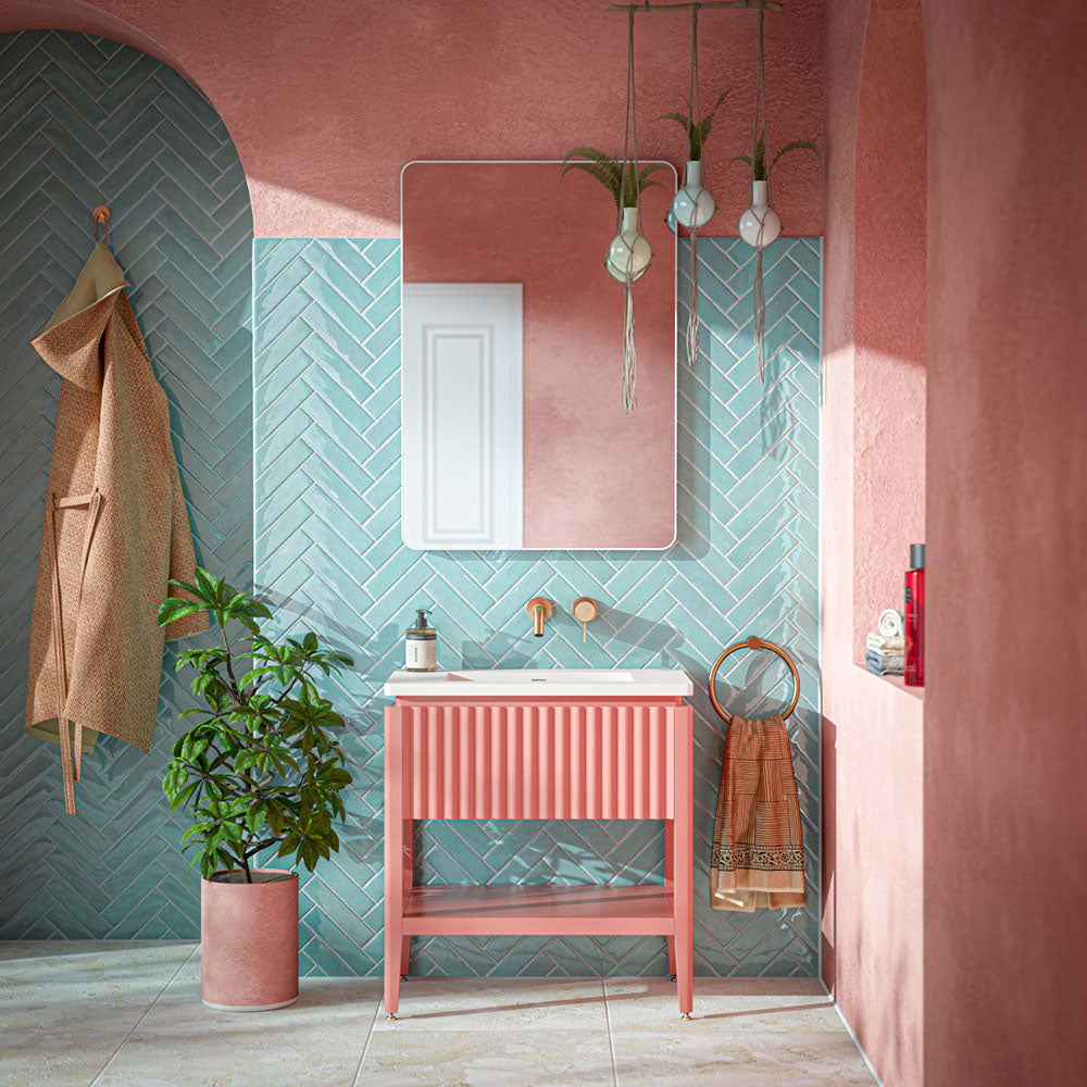 Contemporary bathroom featuring Baresi Puro 3D terrazzo effect porcelain floor tiles, paired with aquamarine glossy herringbone wall tiles, blush pink limewashed walls, a coral fluted vanity, brushed brass fittings and indoor planting for a vibrant, design-led interior.