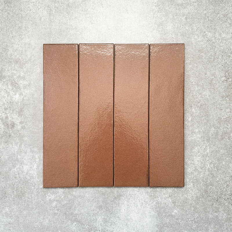 Baroque Cotto porcelain wall and floor tile in a 9.1cm x 37.5cm format, featuring a warm terracotta metallic finish with gently distressed edges, displayed against a textured concrete-effect background.
