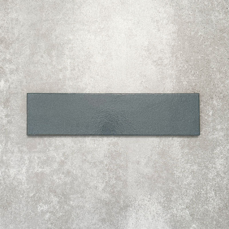 Baroque Laguna Blue porcelain wall and floor tile in a 9.1cm x 37.5cm format, featuring a deep blue metallic finish with gently distressed edges, displayed against a textured concrete-effect background.