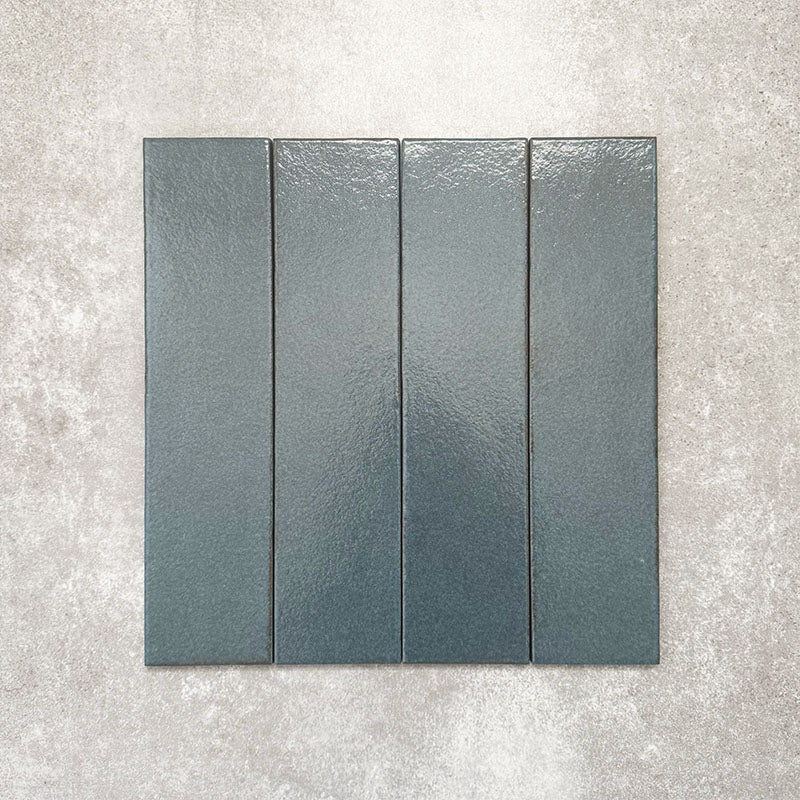 Baroque Laguna Blue porcelain wall and floor tile in a 9.1cm x 37.5cm format, featuring a deep blue metallic finish with gently distressed edges, displayed against a textured concrete-effect background.