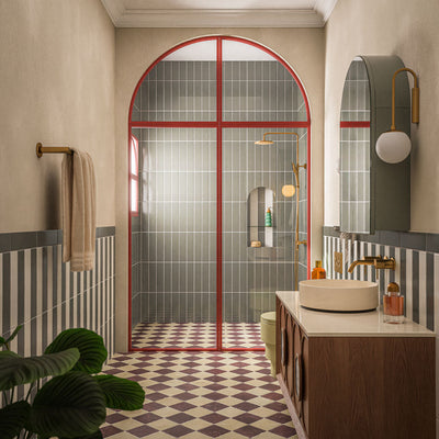 Contemporary bathroom featuring Baroque Lichen Green porcelain wall tiles in a vertical stacked layout, paired with a burgundy and white chequerboard floor, red framed shower screen, brushed brass fittings and a walnut vanity for a bold, design-led interior.