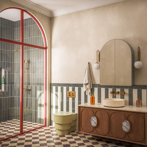 Contemporary bathroom featuring Baroque Lichen Green porcelain wall tiles in a vertical stacked layout, paired with a burgundy and white chequerboard floor, red framed shower screen, brushed brass fittings and a walnut vanity for a bold, design-led interior.