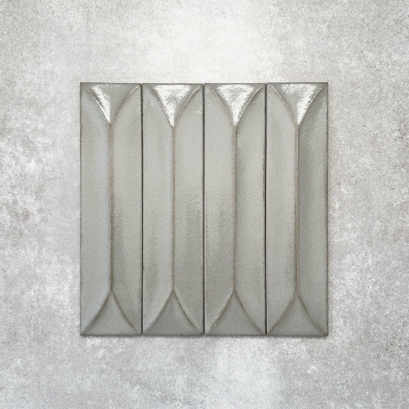 Baroque Decor Lichen Green porcelain wall tile in a 9.1cm x 37.5cm format, featuring a soft sage green metallic finish with a raised geometric relief design and gently distressed edges, displayed against a textured concrete-effect background.
