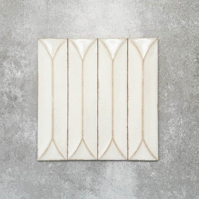 Baroque Decor Vanilla porcelain wall tile in a 9.1cm x 37.5cm format, featuring a soft cream metallic finish with a raised geometric relief design and gently distressed edges, displayed against a textured concrete-effect background.