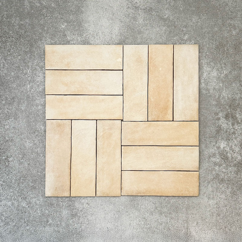 Flat lay of Zellige Arena Marfil Brick 6.5 × 20cm Moroccan-style ceramic tiles, shown in a warm beige and cream colour palette with subtle tonal variation and gently uneven edges, arranged in a basketweave layout on a textured grey background to highlight the handcrafted, zellige-effect finish.