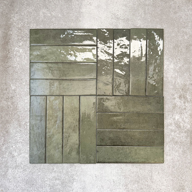 Nomad Sage Green brick wall tiles in a 6 × 24.6cm format, shown in a basketweave arrangement with a glossy, lightly textured surface and deep green tones, ideal for creating an industrial-style wall finish.