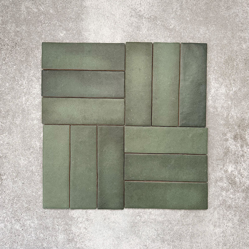 Flat lay of Zellige Malachite Green 6.5×20cm Moroccan-style ceramic brick tiles, arranged in a basketweave layout, showcasing subtle tonal variation, handmade-look texture and rich green glaze on a neutral background.