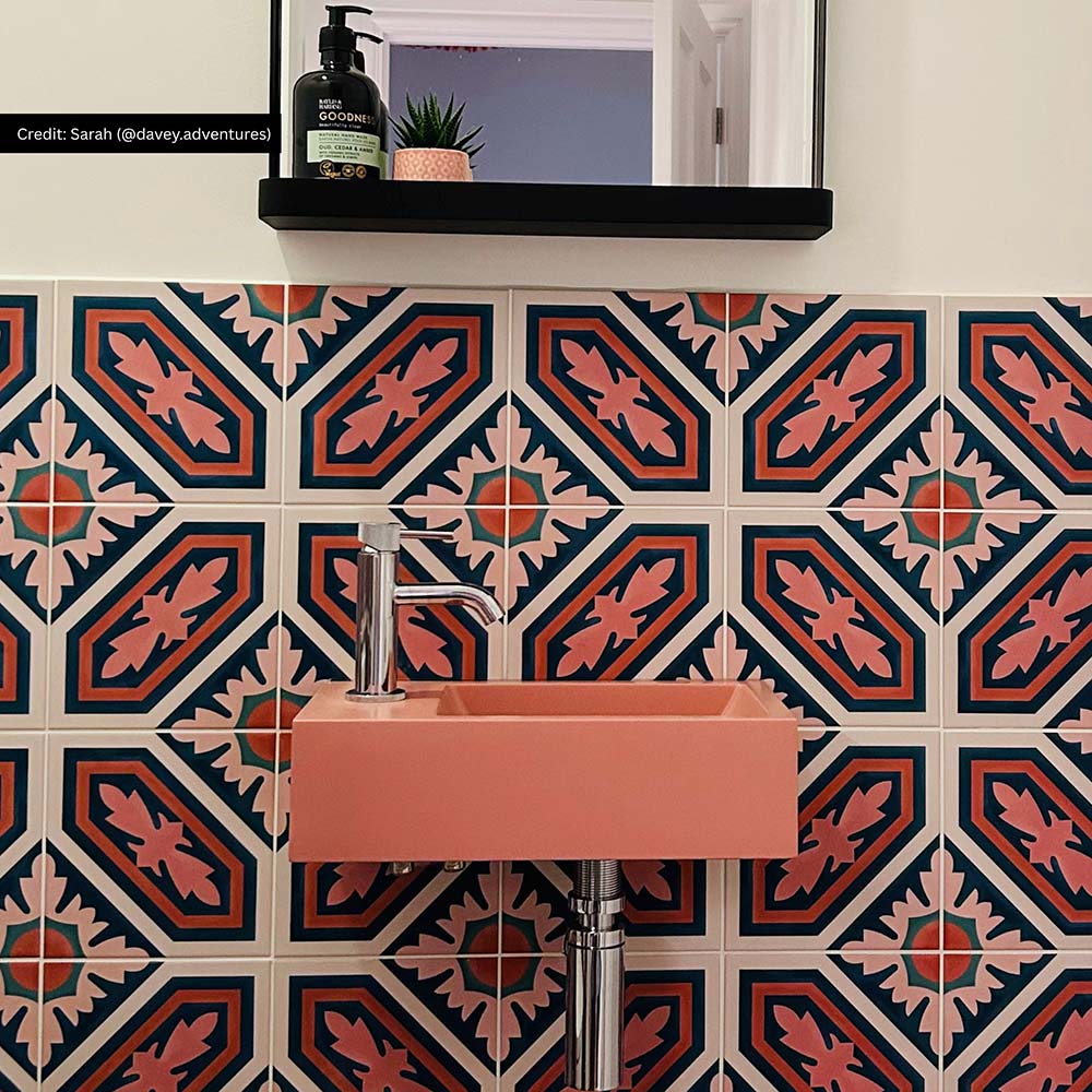 Bathroom interior featuring London Streets Conduit Street 20x20cm Victorian Moroccan style wall tiles, styled with a pink basin sink, chrome tap and black mirror shelf, creating a bold patterned bathroom feature wall.