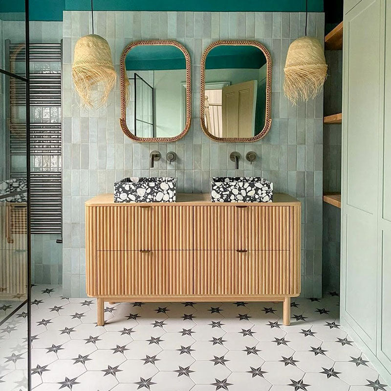 Bathroom featuring Zellige Aqua 6.5×20cm Moroccan-style ceramic brick tiles installed on the walls behind a double vanity, showcasing soft blue-green tonal variation and a handmade-look finish, styled with a fluted wooden unit, patterned floor tiles and woven pendant lighting.