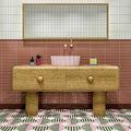 Bathroom interior featuring Abstract Serit Patterned Tiles in a 20x20cm format, laid as a bold geometric floor design. The repeating pattern combines soft pink, deep green and crisp white tones with striped detailing, paired with a wooden vanity unit and blush basin to create a playful yet contemporary bathroom setting.