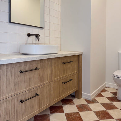 Bathroom interior featuring Fayrouz Rosso 15.2x15.2cm natural marble tiles with a tumbled finish, installed in a chequerboard floor with light marble, styled with a wooden vanity unit, round basin and neutral walls.