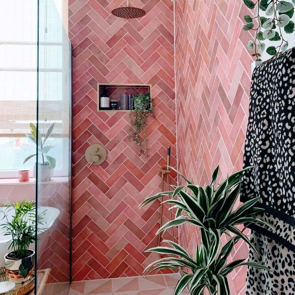 Bathroom wall featuring Zellige Rose Pink Brick 6.5 × 20cm Moroccan-style ceramic tiles, laid in a herringbone pattern with soft blush and dusty pink tones, paired with brass wall lights and taps, a green painted door and arched mirror to create a warm, characterful and handcrafted zellige-effect finish.