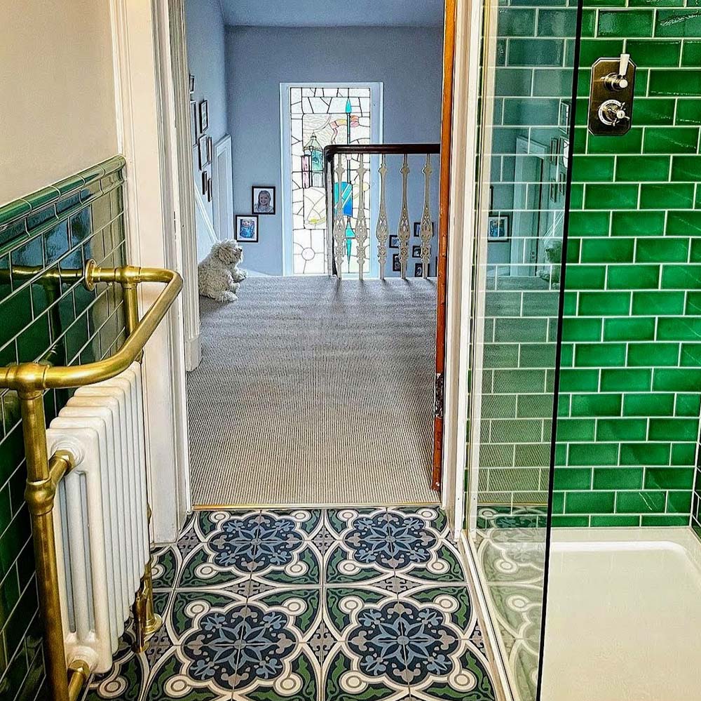 Bathroom interior featuring London Streets Baker Street 20x20cm Victorian Moroccan style floor tiles, styled with glossy green metro wall tiles, brass towel rail and glass shower enclosure, creating a decorative patterned bathroom floor.