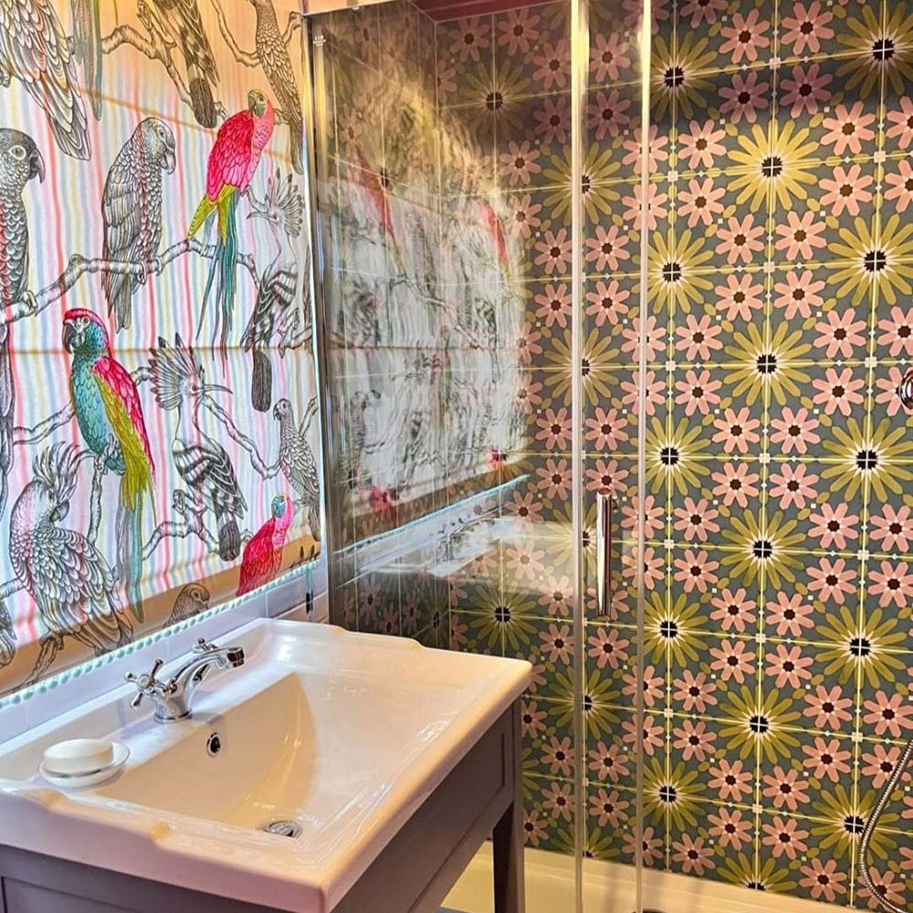 Bathroom shower wall featuring Fez Summer 20x20cm Moroccan-style porcelain tiles, showcasing a vibrant geometric star pattern in soft green, blue and blush pink tones, paired with a white basin, glass shower screen and bold patterned wallpaper for a colourful, eclectic finish.