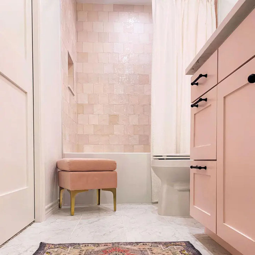 Bathroom featuring Zellige Pink Mist Square 13.2 × 13.2cm Moroccan-style ceramic wall tiles in soft pale pink tones, laid in a neat grid around a bath area, paired with blush cabinetry, white fittings and subtle metallic accents for a calm, elegant zellige-effect finish.