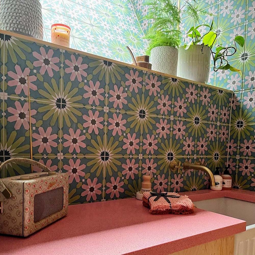 Bathroom vanity splashback featuring Fez Summer 20x20cm Moroccan-style porcelain tiles, showcasing a colourful geometric star pattern in soft green, blue and blush pink tones, paired with a pink worktop, brass tapware and indoor plants for a bold, characterful finish.