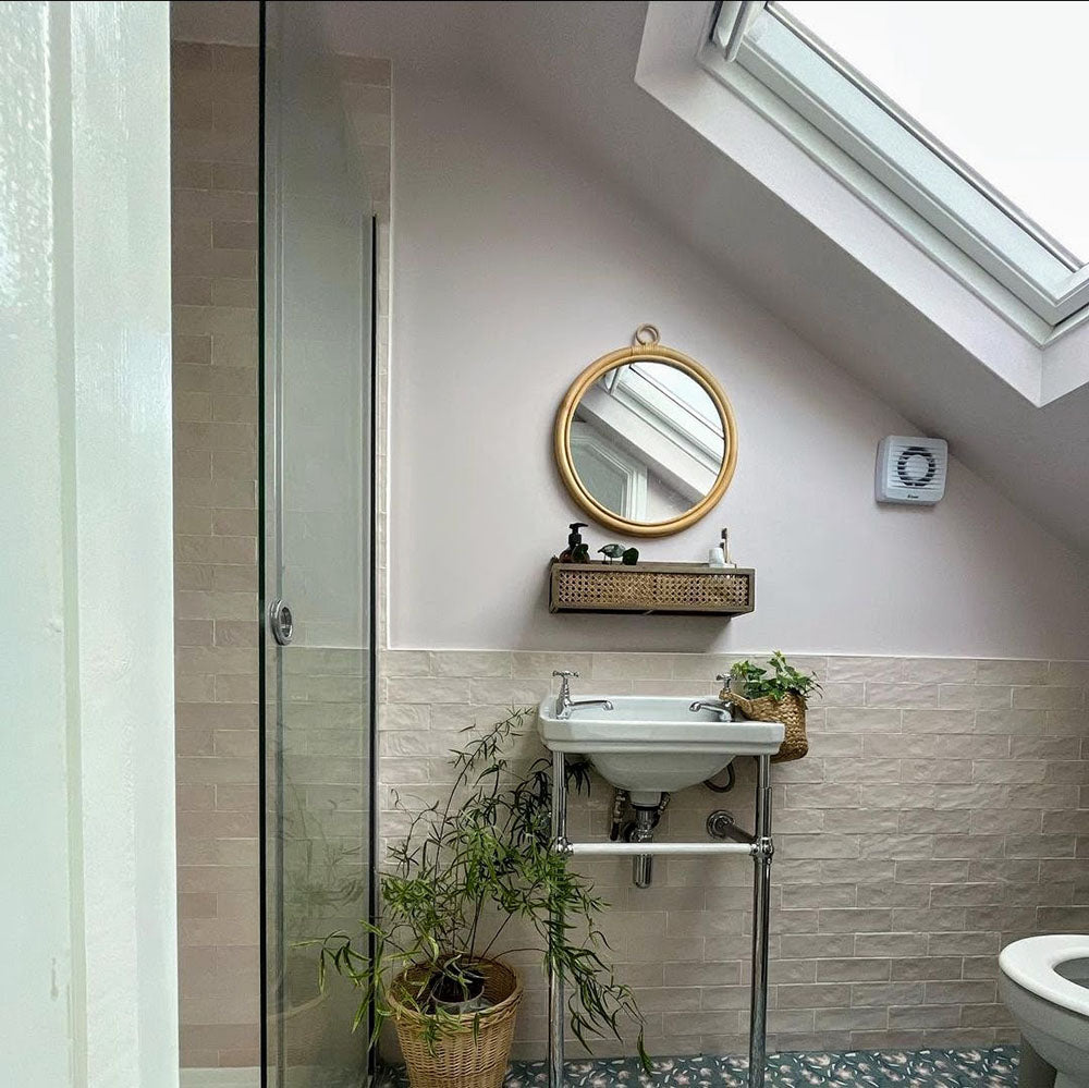 Bathroom featuring Zellige Pink Mist Brick 6.5 × 20cm Moroccan-style ceramic wall tiles in soft pale pink tones, installed in a horizontal brick layout as a half-height wall finish, paired with a wall-mounted basin, chrome fittings and botanical accents for a light, calming zellige-effect look.