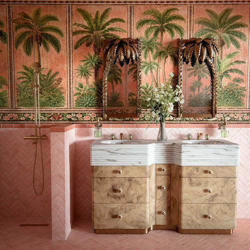 Bathroom featuring Benomar Pink Moroccan Mini Brick Matt 5x15cm wall tiles in a herringbone layout, styled with tropical palm wallpaper, carved wood mirrors, and marble-effect basins for a luxurious eclectic interior.