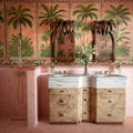 Bathroom featuring Benomar Pink Moroccan Mini Brick Matt 5x15cm wall tiles in a herringbone layout, styled with tropical palm wallpaper, carved wood mirrors, and marble-effect basins for a luxurious eclectic interior.