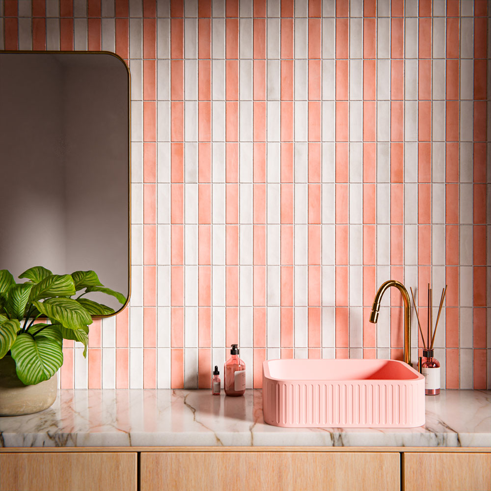 Bathroom vanity area featuring Benomar Moroccan-style brick tiles in soft blush and ivory tones, installed vertically as a statement wall, styled with a fluted pink basin, brushed brass tap, marble surface, and greenery.