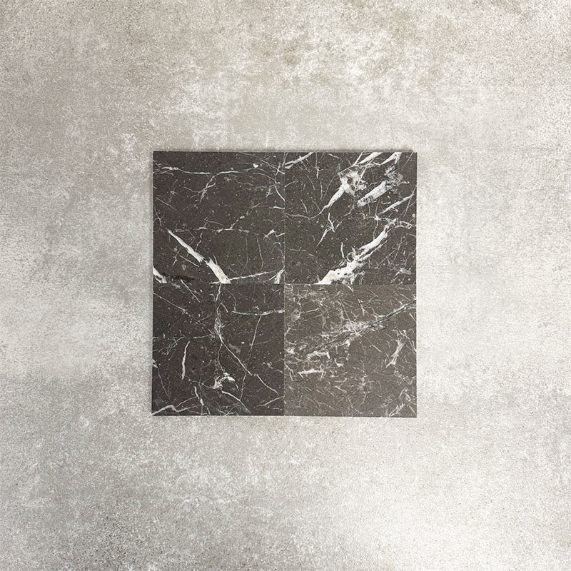 Four Fayrouz Black 15.2x15.2cm natural marble tiles with a honed finish arranged together, showcasing deep black tones, bold white veining and natural variation against a neutral textured background.
