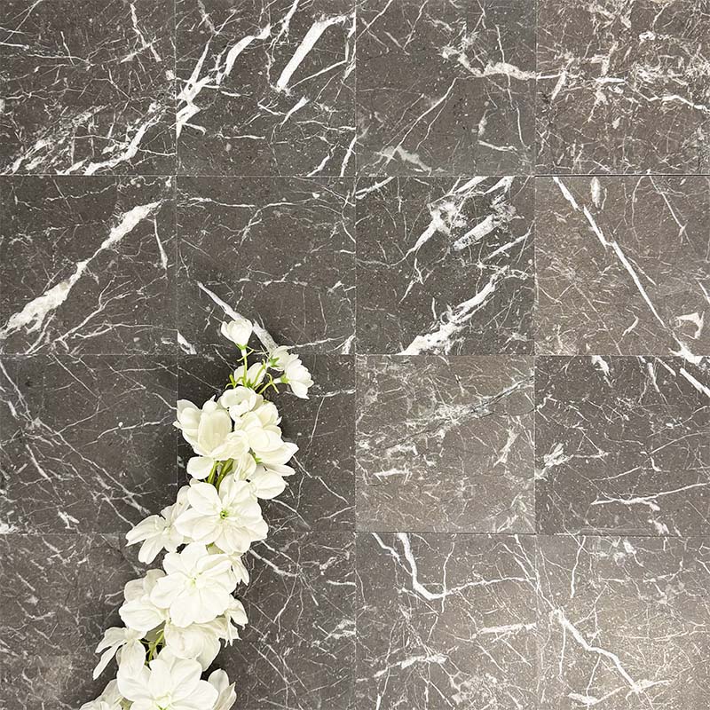 Flat lay of Fayrouz Black 15.2x15.2cm natural marble tiles with a honed finish, featuring deep charcoal tones and bold white veining, styled with soft white flowers for contrast and texture.