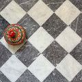 Chequerboard layout featuring Fayrouz Black 15.2x15.2cm natural marble tiles with a tumbled finish, paired with white marble tiles, installed diagonally and styled with a decorative patterned dish for contrast.