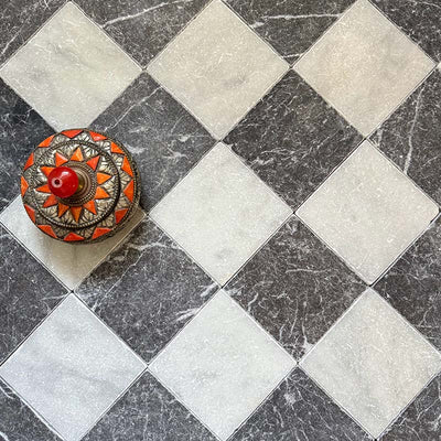 Chequerboard layout featuring Fayrouz Black 15.2x15.2cm natural marble tiles with a tumbled finish, paired with white marble tiles, installed diagonally and styled with a decorative patterned dish for contrast.