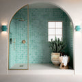 Contemporary walk-in shower featuring Bora Bora Aqua Square 10cm x 10cm flux glaze wall tiles, paired with white floor tiles, brass shower fittings and an arched alcove for a bright Mediterranean-inspired bathroom.