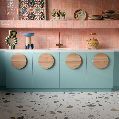 Kitchen featuring Byblos Cotton 60x120cm terrazzo-effect porcelain floor tiles, paired with blush pink Moroccan-style wall tiles, pastel blue cabinetry, and brass fixtures for a playful contemporary interior.