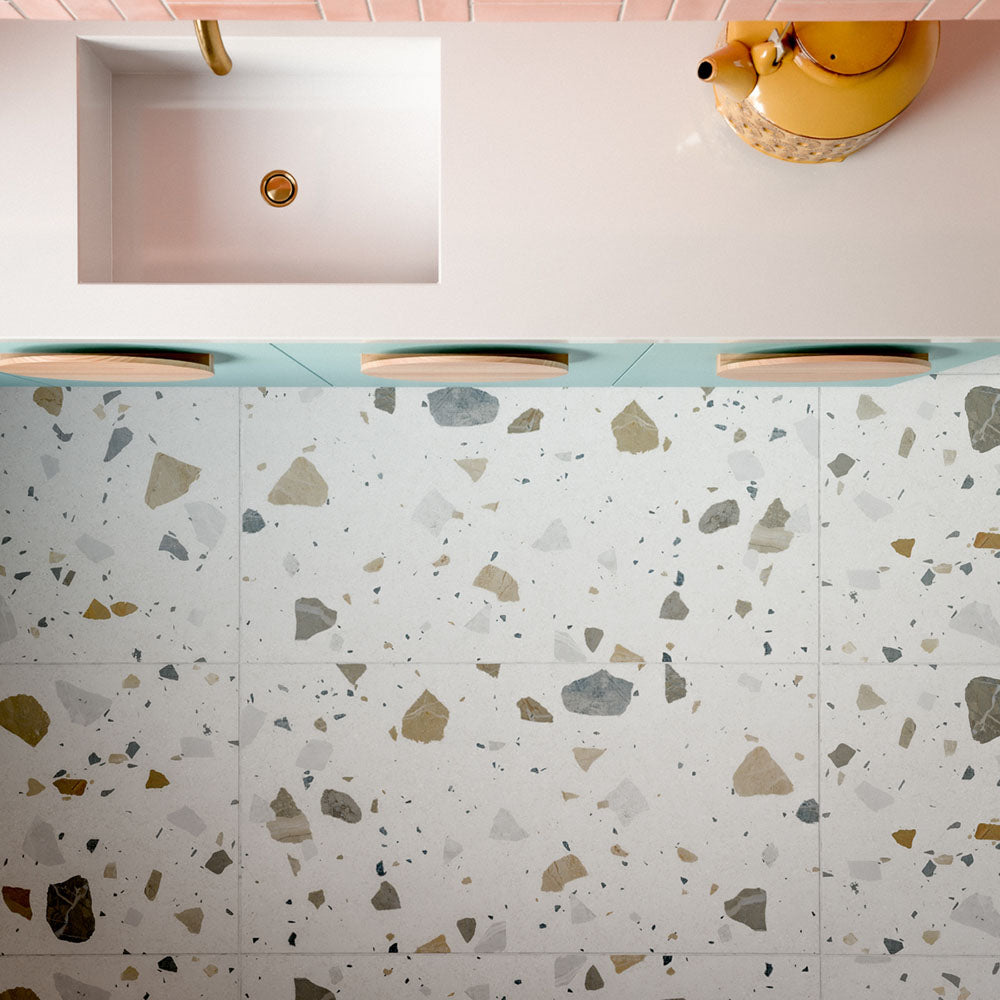 Kitchen featuring Byblos Cotton 60x120cm terrazzo-effect porcelain floor tiles, paired with blush pink Moroccan-style wall tiles, pastel blue cabinetry, and brass fixtures for a playful contemporary interior.