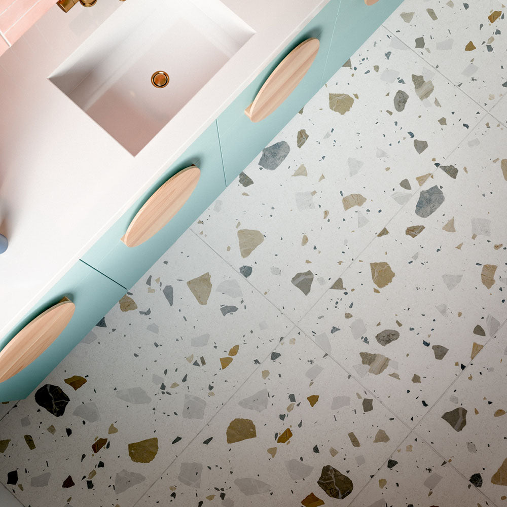Kitchen featuring Byblos Cotton 60x120cm terrazzo-effect porcelain floor tiles, paired with blush pink Moroccan-style wall tiles, pastel blue cabinetry, and brass fixtures for a playful contemporary interior.