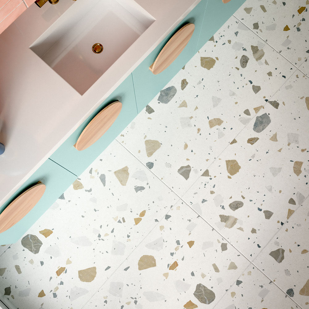 Kitchen featuring Byblos Cotton 60x120cm terrazzo-effect porcelain floor tiles, paired with blush pink Moroccan-style wall tiles, pastel blue cabinetry, and brass fixtures for a playful contemporary interior.