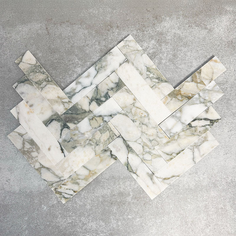 Arrangement featuring Fayrouz Calacatta Green 5x20cm natural marble tiles with a honed finish, displayed in a herringbone layout to emphasise directional movement, showcasing distinctive green and gold veining across a soft white marble base for a dynamic, design-led finish.