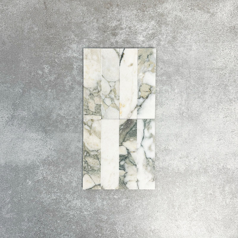 Arrangement featuring Fayrouz Calacatta Green 5x20cm natural marble tiles with a honed finish, displayed in a vertical layout to showcase soft white tones with green and gold veining against a neutral background.